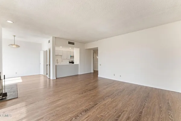 a view of an empty room with wooden floor and a kitchen