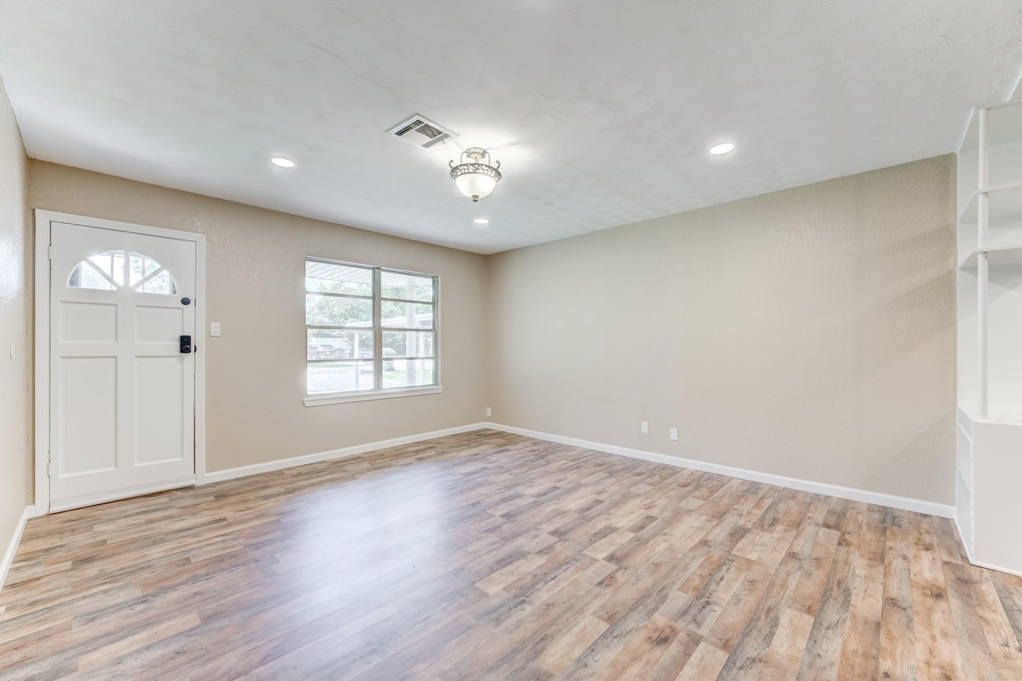 305 Yaupon Street Sweeny, TX 77480 - Photo 18 of 22 This photo showcases a bright and spacious living room with wood laminate flooring, neutral walls, and a central light fixture. It features a classic front door and a large window for natural light, creating an inviting atmosphere.