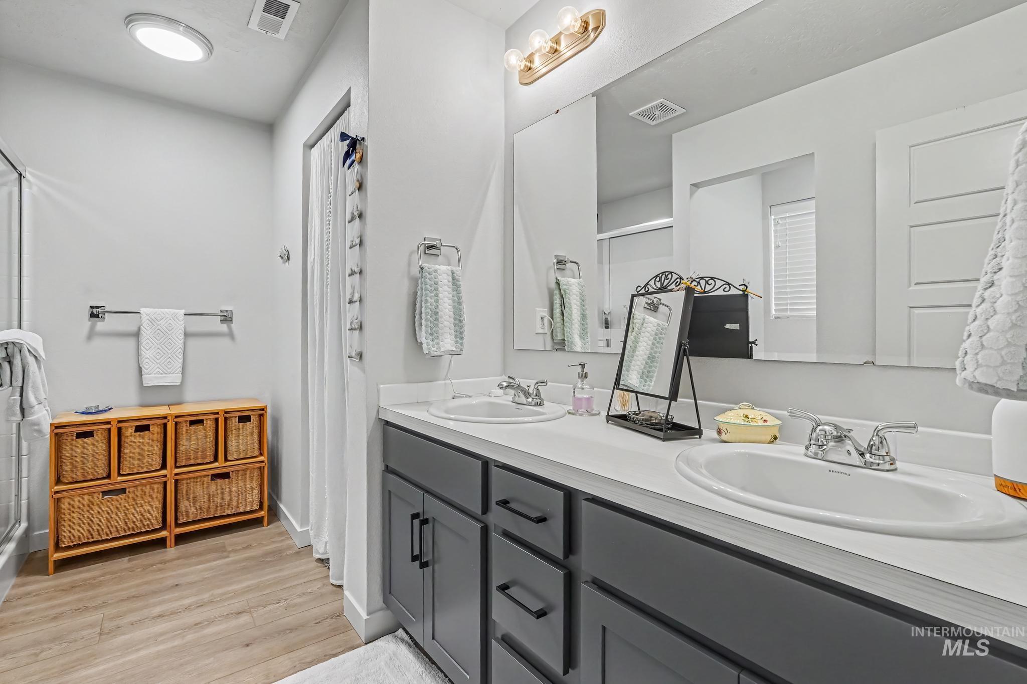 238 West Riggs Spring Avenue Meridian, ID 83642 - Photo 12 of 16 Dual vanity with dark cabinetry, ample counter space, wood-finish flooring, and a walk-in shower