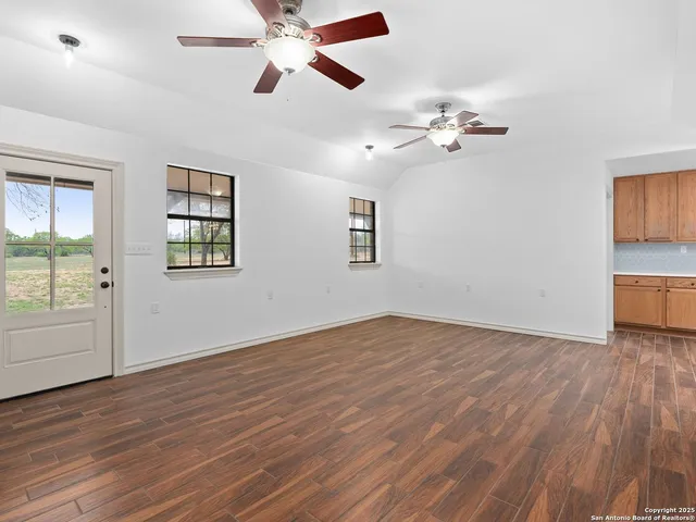 an empty room with wooden floor chandelier fan and windows