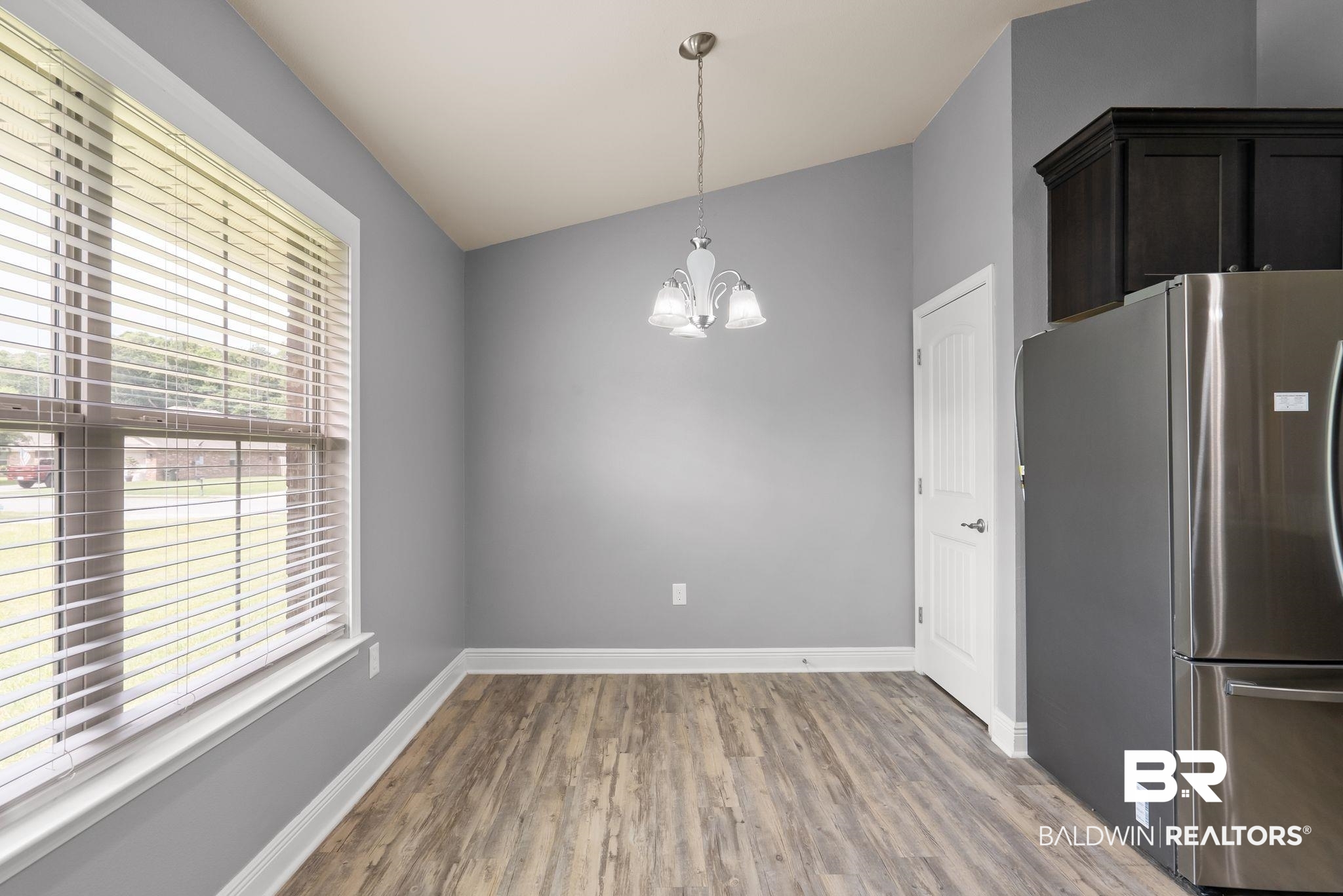 22076 Garland Loop Silverhill, AL 36576 - Photo 9 of 27 Dining area featuring vaulted ceilings, wood-finish flooring, a contemporary chandelier, and a stainless steel refrigerator