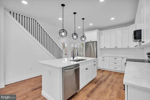 a kitchen with stainless steel appliances a refrigerator a sink dishwasher a stove and white cabinets with wooden floor