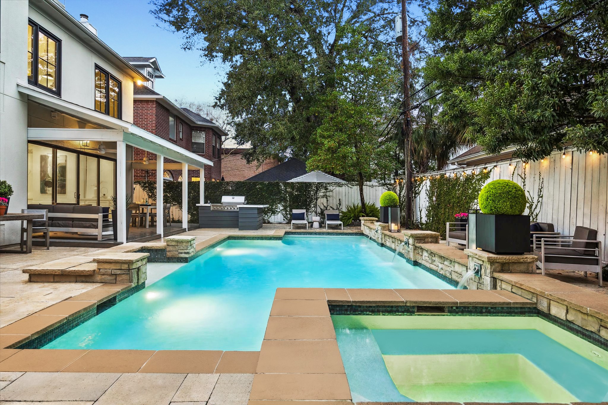 4122 Rice Boulevard West University Place, TX 77005 - Photo 23 of 30 Beautifully designed backyard retreat anchored by a sparkling pool with raised spa and water features. Framed by mature trees and enhanced by multiple seating areas, summer kitchen, and fireside seating, the space offers seamless indoor-outdoor flow and effortless year-round entertaining.