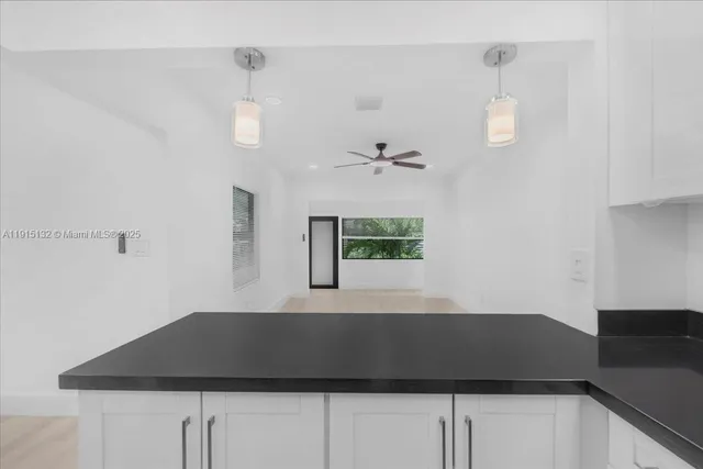an empty room with wooden floor fan and a kitchen view