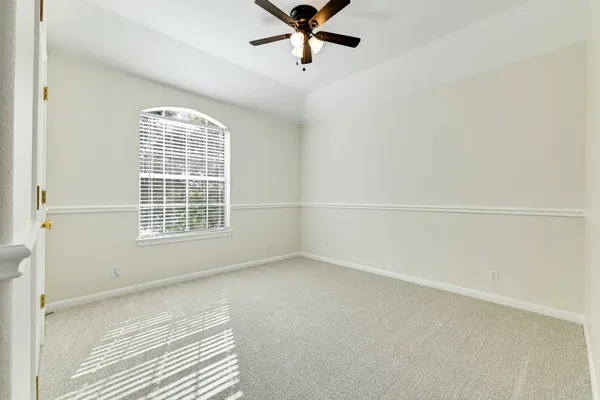 an empty room with a chandelier fan and windows