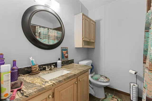 a bathroom with a granite countertop toilet a sink and a mirror