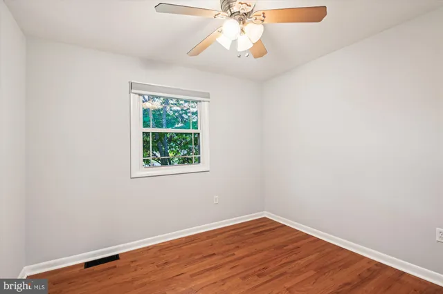 an empty room with wooden floor chandelier fan and windows