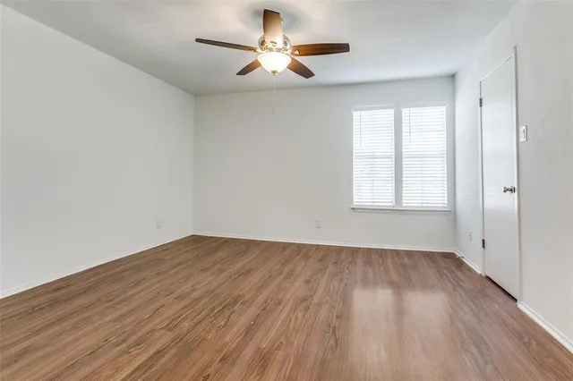an empty room with wooden floor chandelier fan and windows
