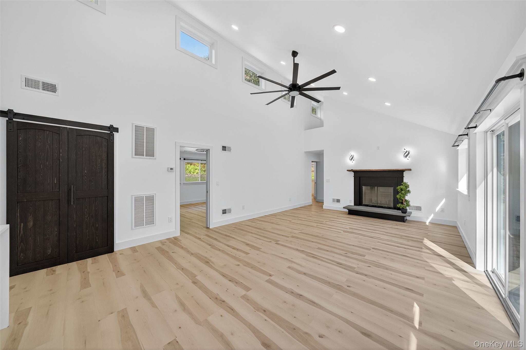 273 Perry Pond Road Narrowsburg, NY 12764 - Photo 13 of 49 Unfurnished living room with a barn door, a glass covered fireplace, high vaulted ceiling, light wood-style flooring, and ceiling fan