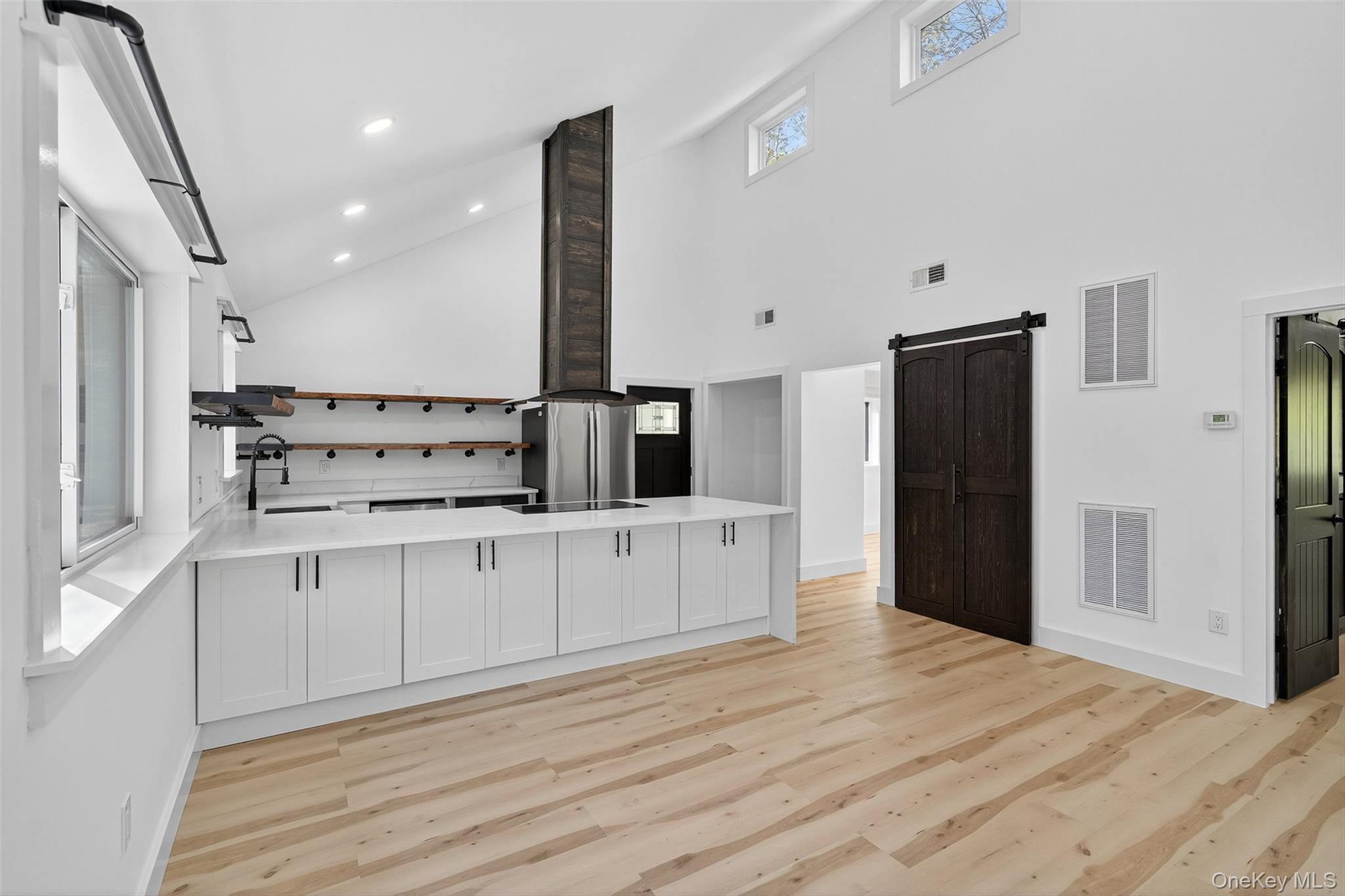 273 Perry Pond Road Narrowsburg, NY 12764 - Photo 22 of 49 Kitchen featuring a barn door, open shelves, light wood-style flooring, high vaulted ceiling, and a peninsula