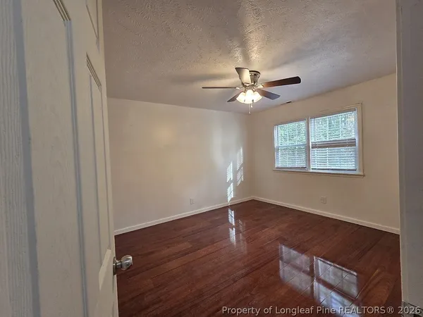 an empty room with wooden floor chandelier fan and windows