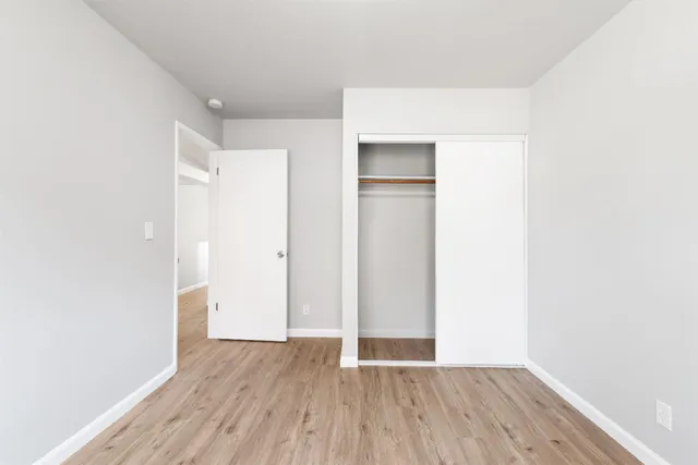 a view of an empty room with wooden floor and closet