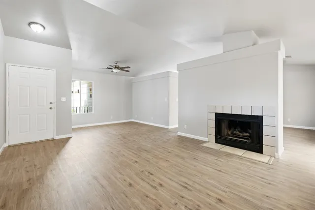 an empty room with wooden floor fireplace and windows