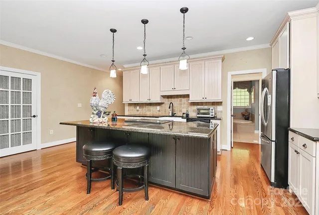 a kitchen with stainless steel appliances granite countertop a refrigerator a sink dishwasher a oven and a dining table with wooden floor