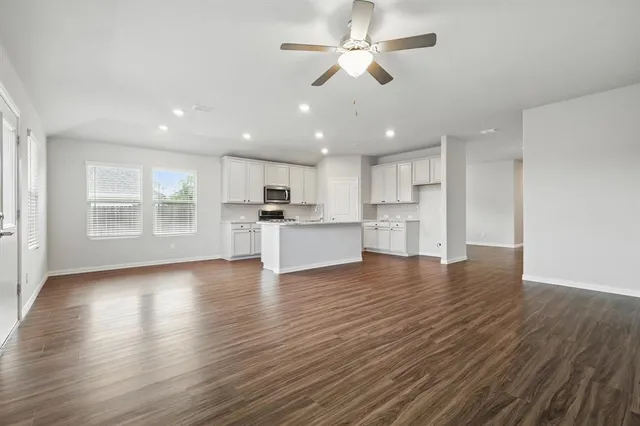 a view of an empty room with wooden floor and a kitchen
