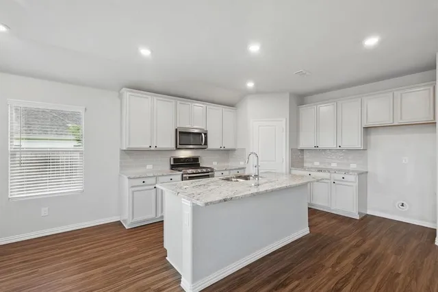 a kitchen with stainless steel appliances white cabinets a sink a stove a refrigerator and microwave