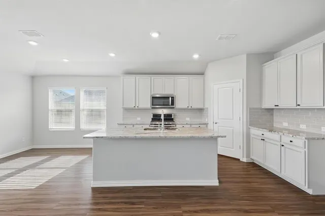 a large kitchen with stainless steel appliances granite countertop a stove a sink dishwasher a refrigerator and white cabinets with wooden floor