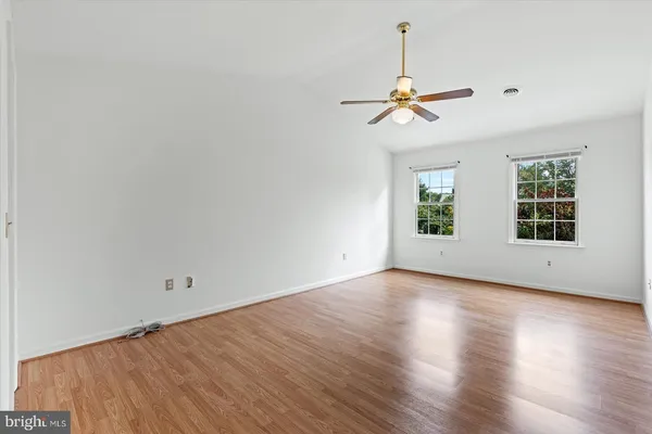 an empty room with wooden floor ceiling fan and windows