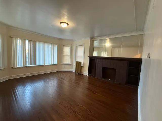 an empty room with wooden floor fireplace and windows