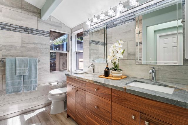 a bathroom with a granite countertop sink a toilet a mirror and shower