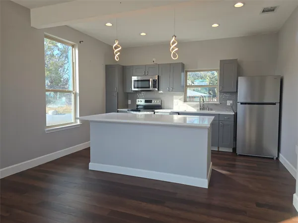 a kitchen with kitchen island a sink a stove a refrigerator and a dining table with wooden floor