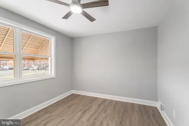 an empty room with wooden floor ceiling fan and windows
