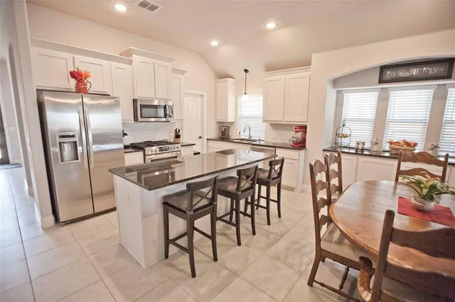 a kitchen with stainless steel appliances kitchen island granite countertop a table chairs sink and cabinets