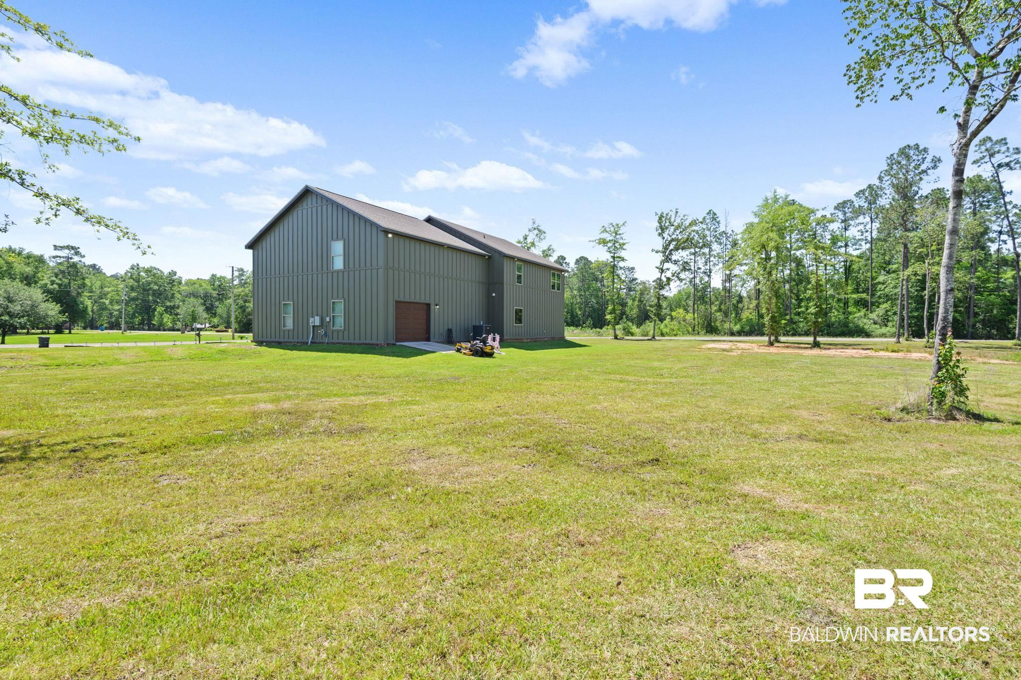 11025 Creax Road Axis, AL 36505 - Photo 7 of 45 Expansive green space surrounds a two-story structure featuring vertical panel siding and a brown garage door