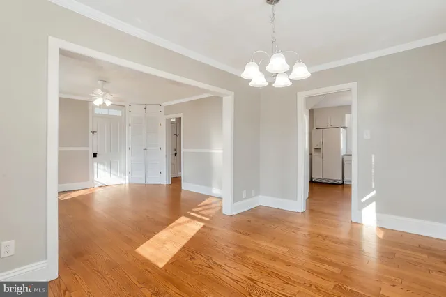 a view of an empty room and kitchen view with wooden floor
