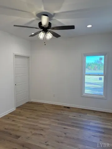 an empty room with wooden floor fan and windows