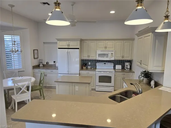 a kitchen with stainless steel appliances granite countertop a stove a sink a refrigerator and a dining table with white cabinets