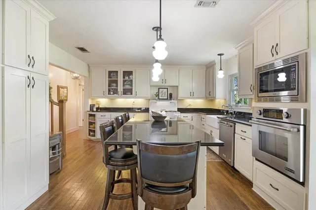a kitchen with stainless steel appliances granite countertop a stove top oven a refrigerator a sink dishwasher a dining table and chairs with wooden floor