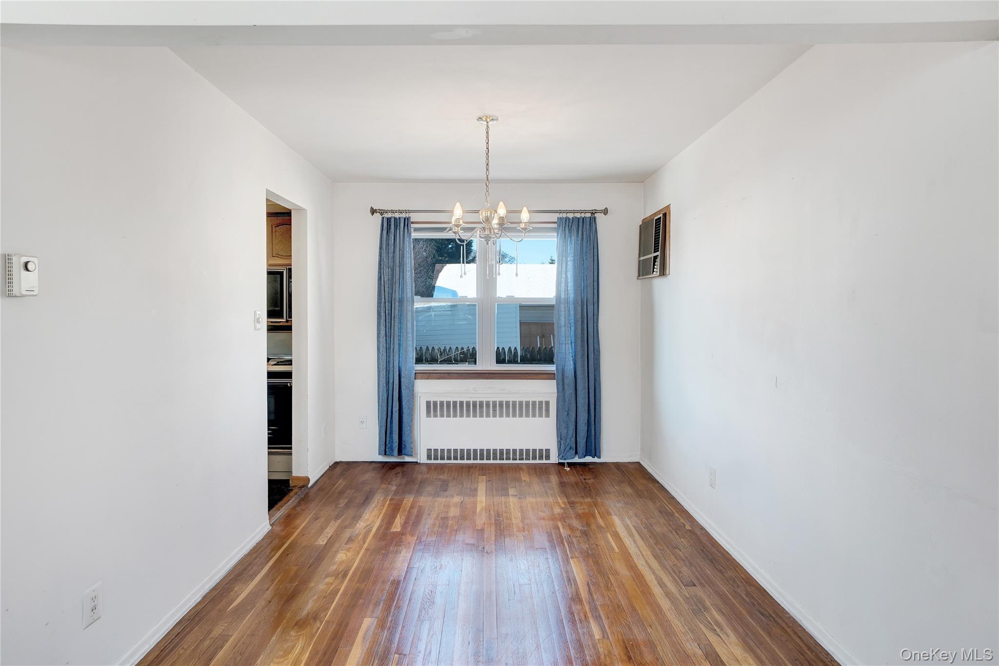 212 Newbridge Road Hicksville, NY 11801 - Photo 5 of 18 Unfurnished dining area featuring radiator, a chandelier, and hardwood / wood-style floors