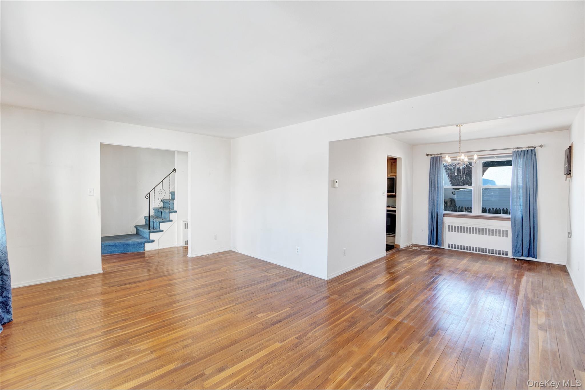 212 Newbridge Road Hicksville, NY 11801 - Photo 7 of 18 Spare room featuring a chandelier, radiator heating unit, stairway, and light wood-type flooring