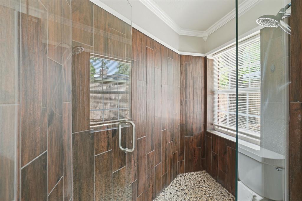 1108 Billie Ruth Lane Hurst, TX 76053 - Photo 15 of 27 Walk-in shower featuring wood-finish wall tiling, a pebble-finish floor, and a frameless glass enclosure