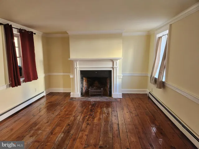 a view of an empty room with wooden floor fireplace and a window