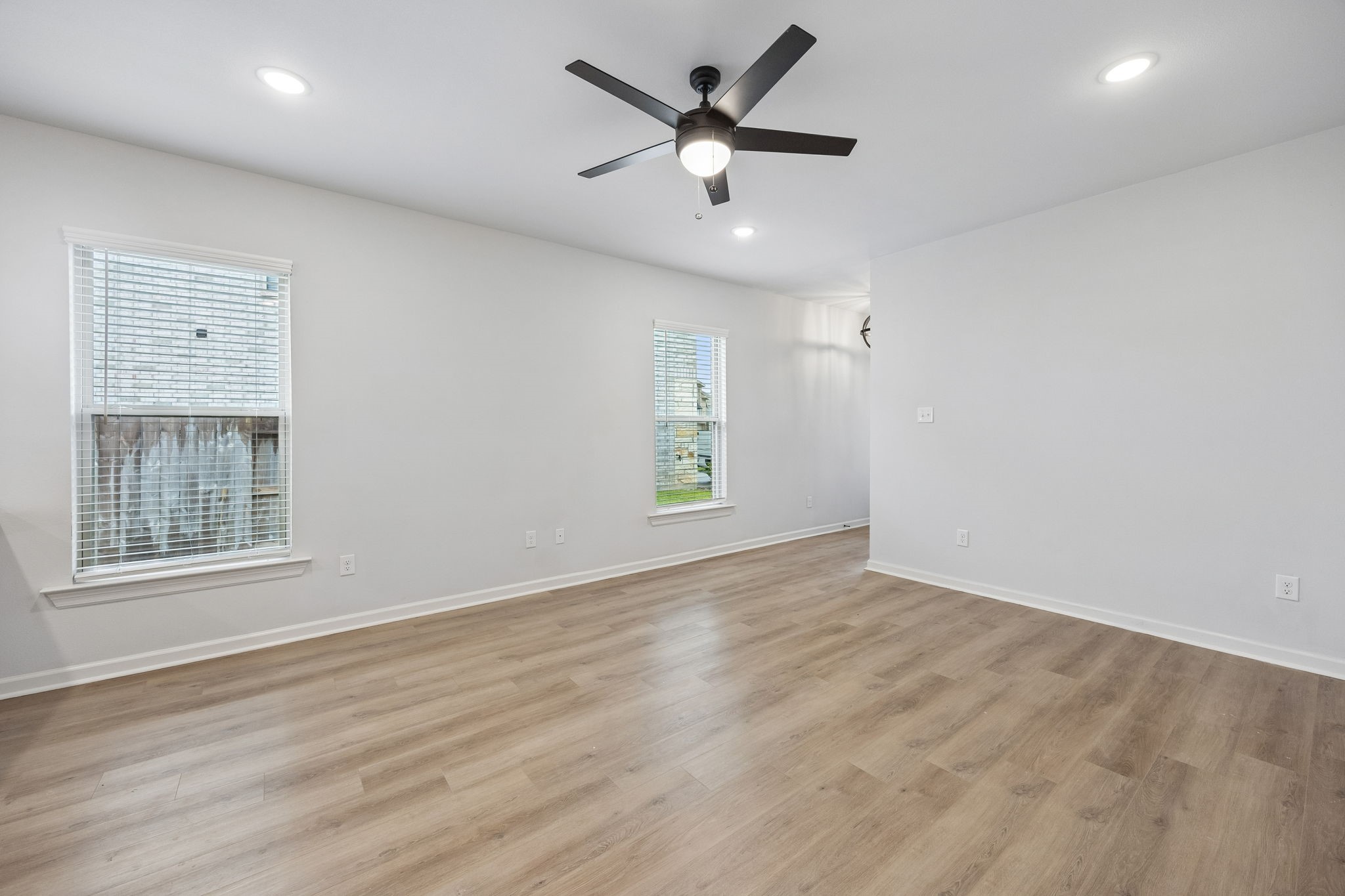 10902 Bonfire Trail Beasley, TX 77417 - Photo 4 of 36 This photo shows a bright, spacious room with light vinyl plank flooring, neutral walls, and two large windows. There is a modern ceiling fan and recessed lighting, creating a fresh and inviting atmosphere.