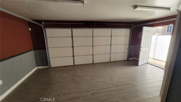 an empty room with wooden floor and way to kitchen