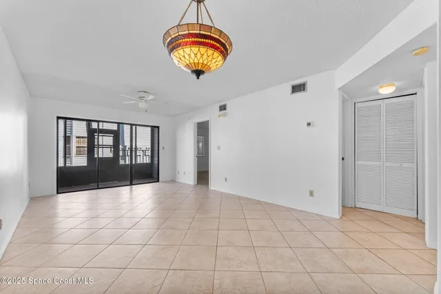 a view of an empty room with window and chandelier fan