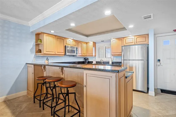 a kitchen with stainless steel appliances granite countertop a refrigerator a sink dishwasher a stove and a dining table with wooden cabinet