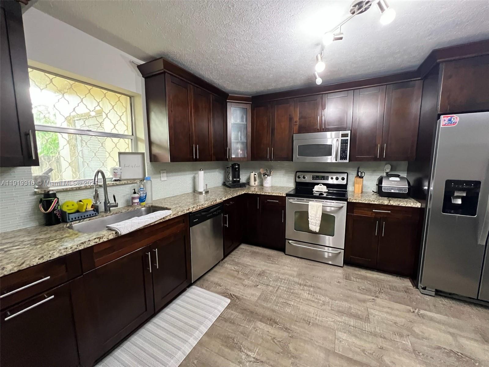 8423 Southwest 137th Avenue, Unit 8423 Miami, FL 33183 - Photo 3 of 3 a kitchen with stainless steel appliances granite countertop wooden cabinets a refrigerator a sink a stove a microwave and wooden floors