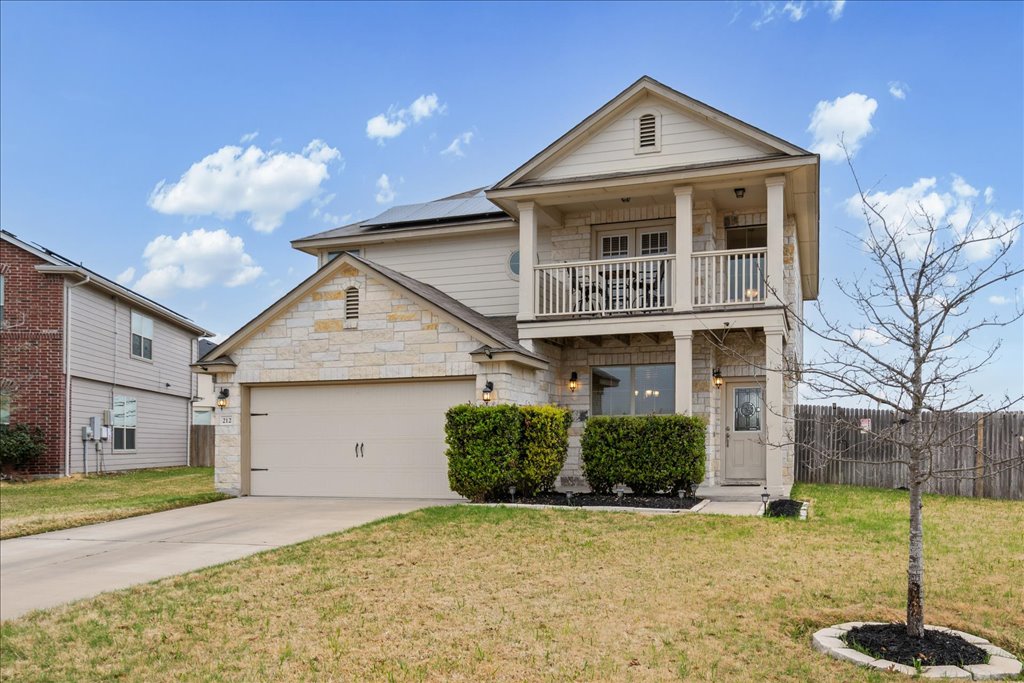 212 Plata Lane Jarrell, TX 76537 - Photo 2 of 30 View of front of property with solar panels, stone siding, concrete driveway, an attached garage, and a balcony