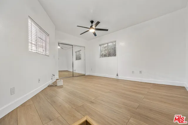 an empty room with wooden floor ceiling fan and windows