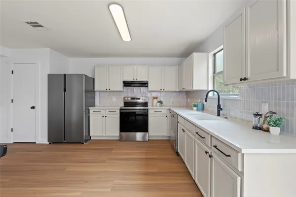 a kitchen with stainless steel appliances a refrigerator a sink a stove and white cabinets