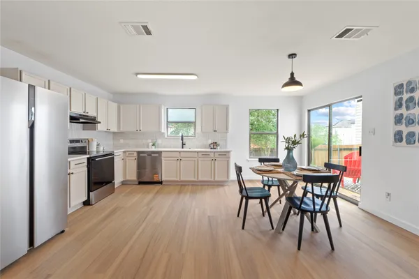 a kitchen with a table chairs a sink dishwasher a refrigerator and cabinets with wooden floor