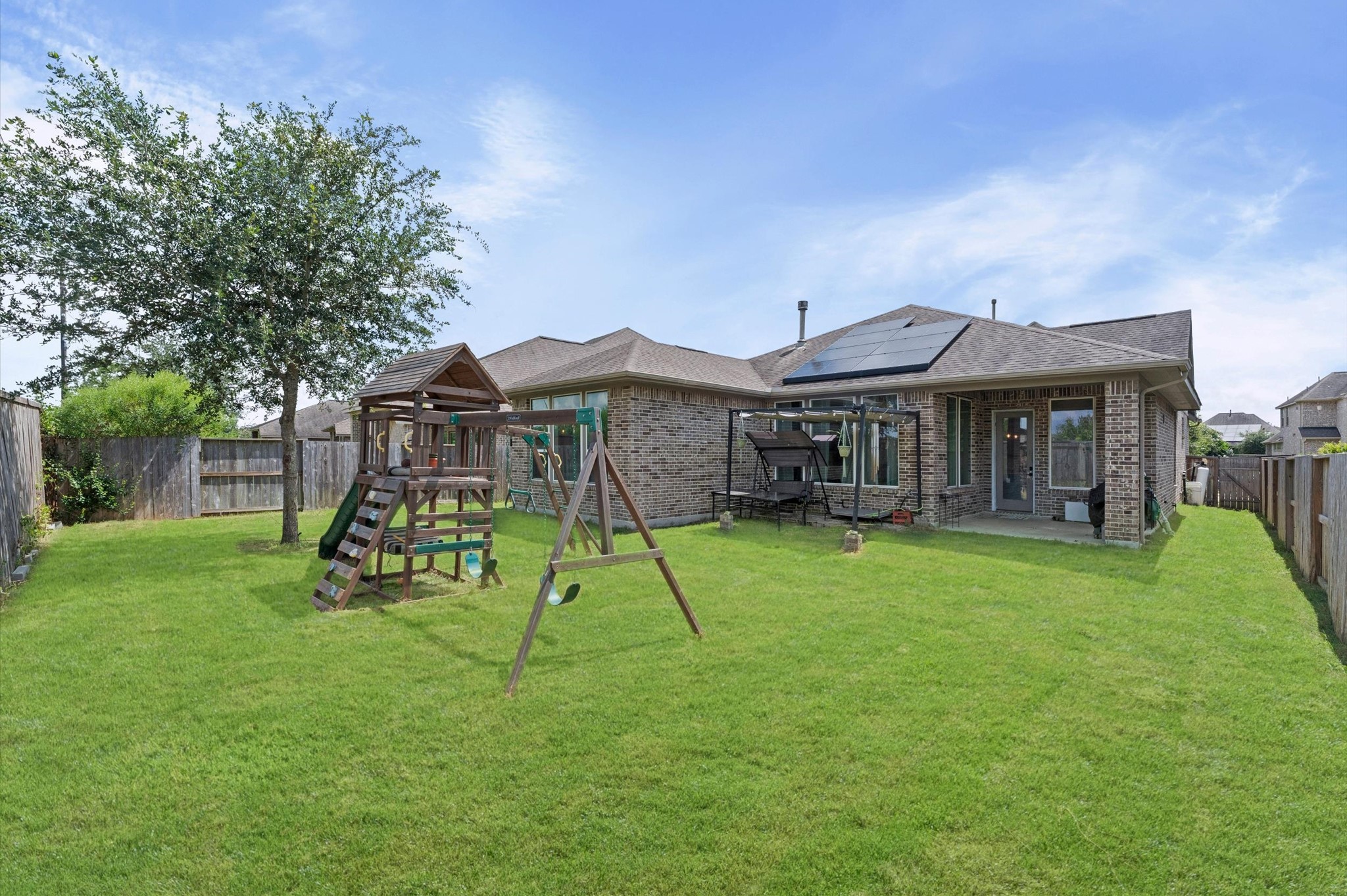 3510 Whitman Drive Rosharon, TX 77583 - Photo 17 of 25 Spacious backyard with a playset and swing. Features a brick exterior, covered patio, and solar panels on the roof. Perfect for outdoor entertaining and eco-friendly living.