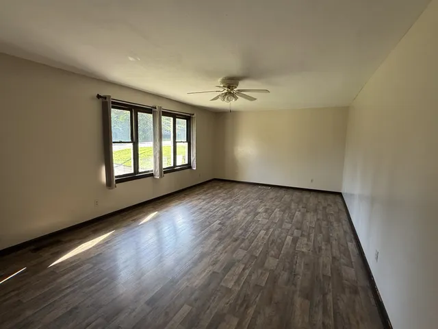 an empty room with wooden floor chandelier fan and windows
