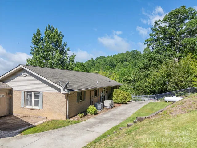 a view of a white house with a yard plants and large tree