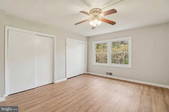 an empty room with wooden floor chandelier fan and windows