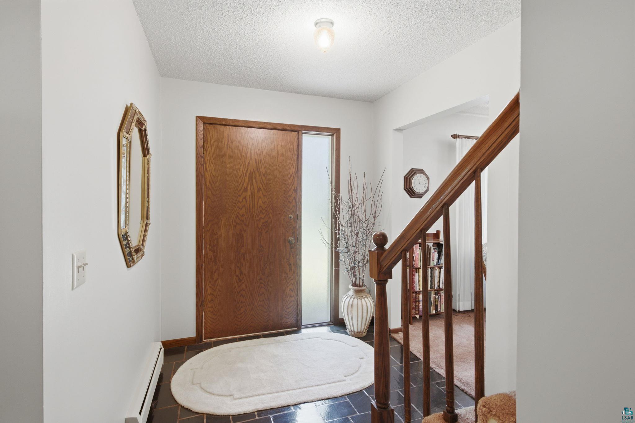 27485 South Kane Road Ashland, WI 54806 - Photo 2 of 35 Entryway featuring a wood-panel door with frosted glass sidelight, dark tile flooring, and a wood staircase with balusters